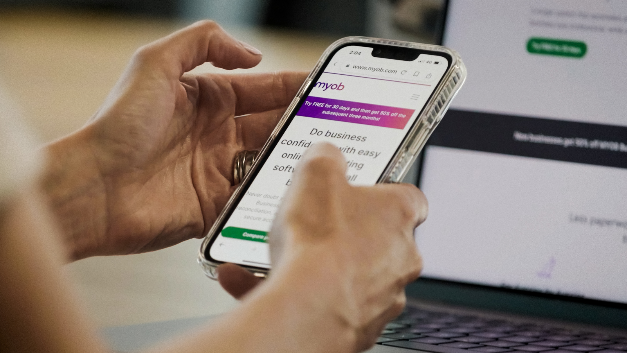 Close up image of hands holding a smart phone while using the MYOB website
