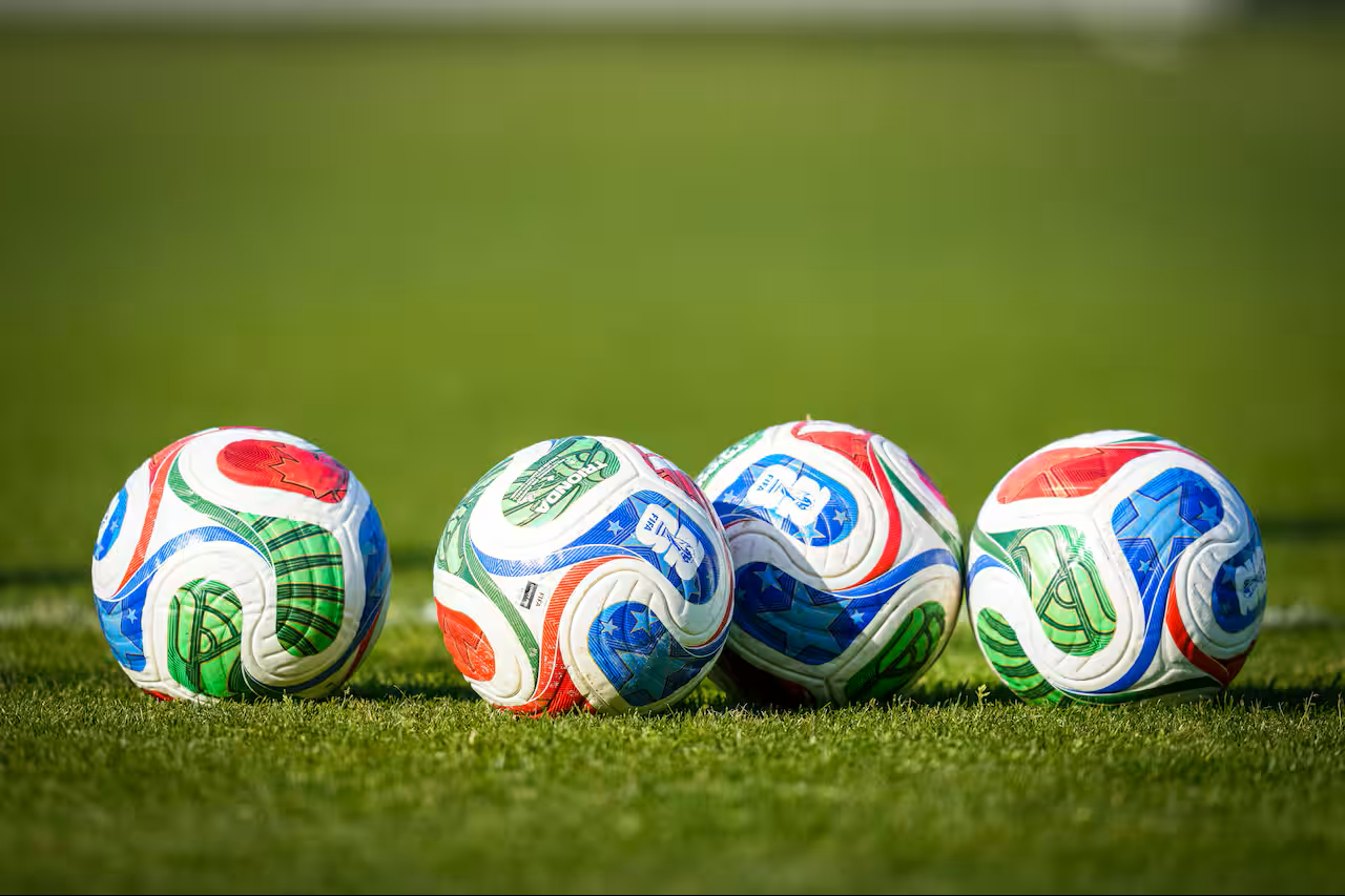 Four Trionda World Cup balls sit on a grass football pitch.