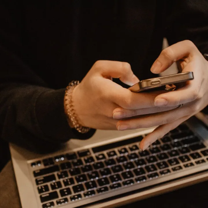 Person using mobile phone with laptop in background.